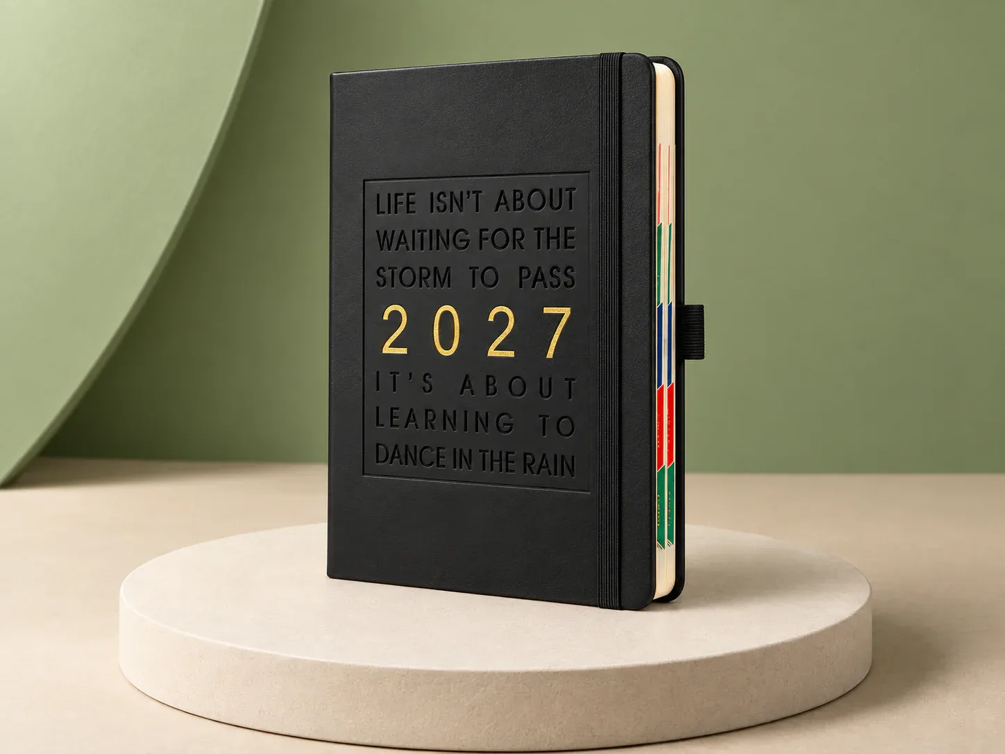 Agenda com elástico e frase na capa, na cor preto, sem personalização: agenda de capa preta com elástico, porta-caneta lateral, divisórias coloridas e frase em inglês em baixo-relevo com 2027 dourado no centro