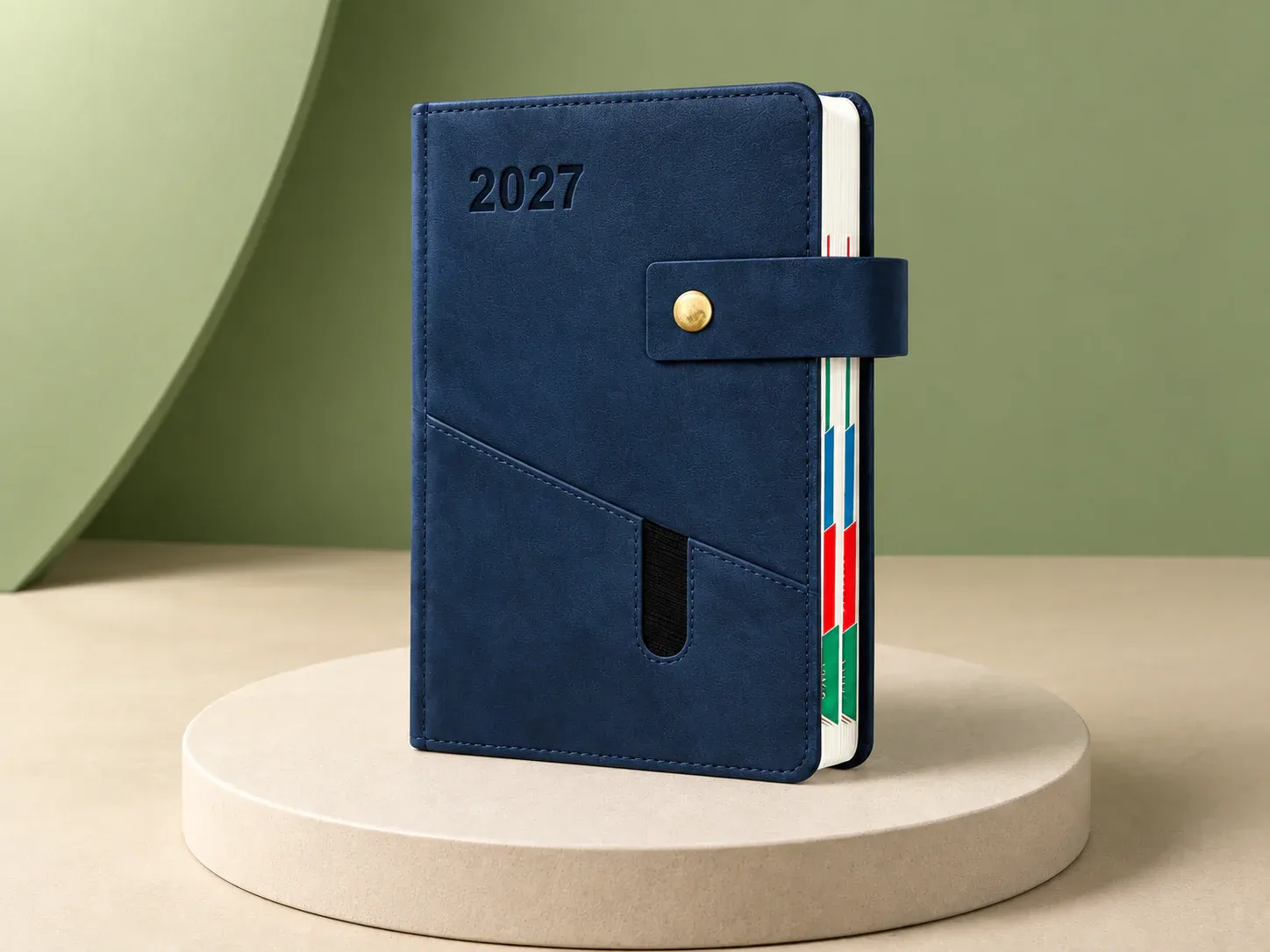 Agenda com fecho de botão e bolso, na cor azul-marinho, sem personalização: agenda de capa azul-marinho costurada, com fecho de botão dourado em aba, bolso diagonal com porta-caneta elástico e divisórias coloridas