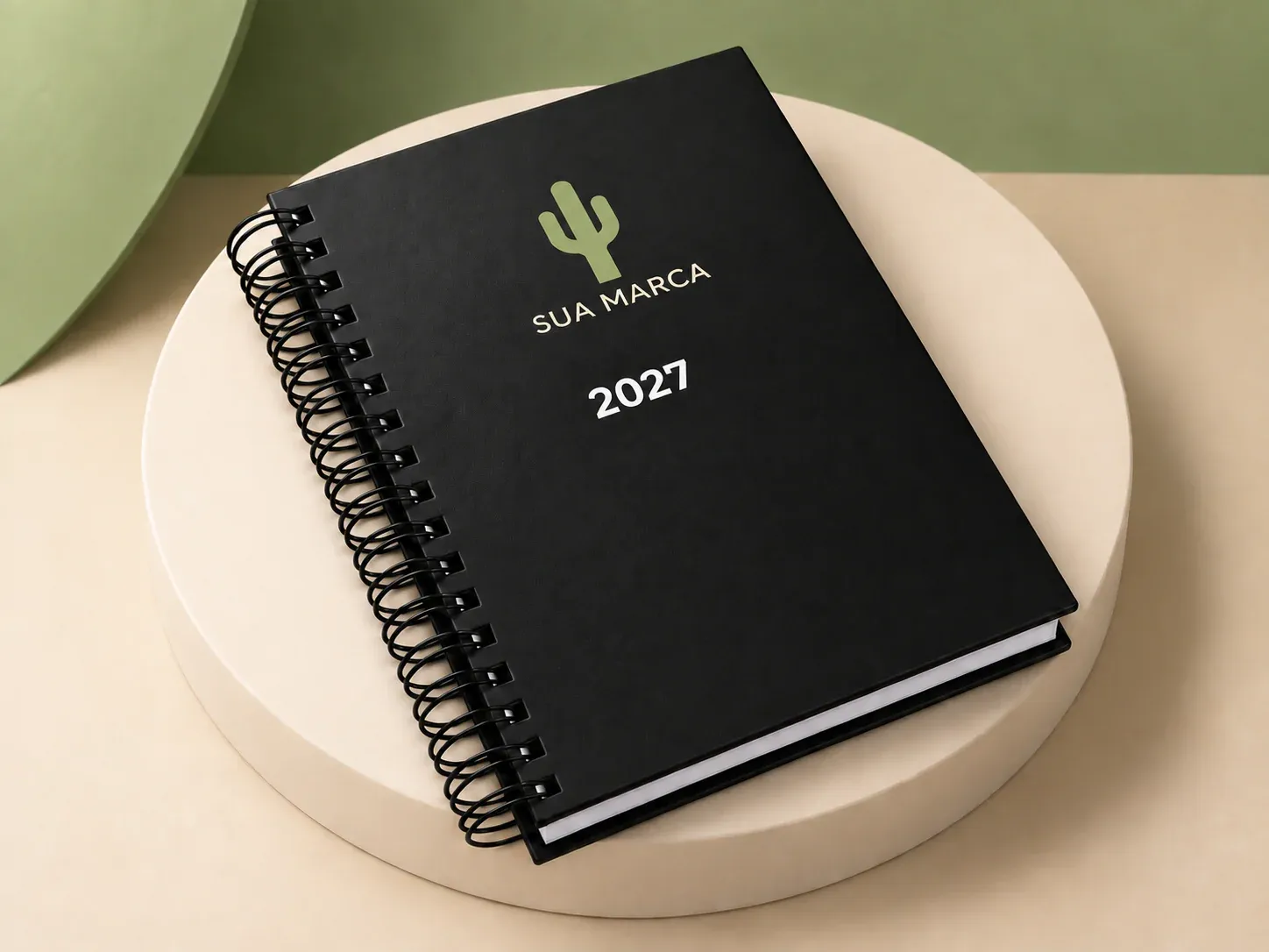 Agenda preta com espiral, com exemplo de personalização colorida: um cacto e o texto “SUA MARCA” impressos em cor