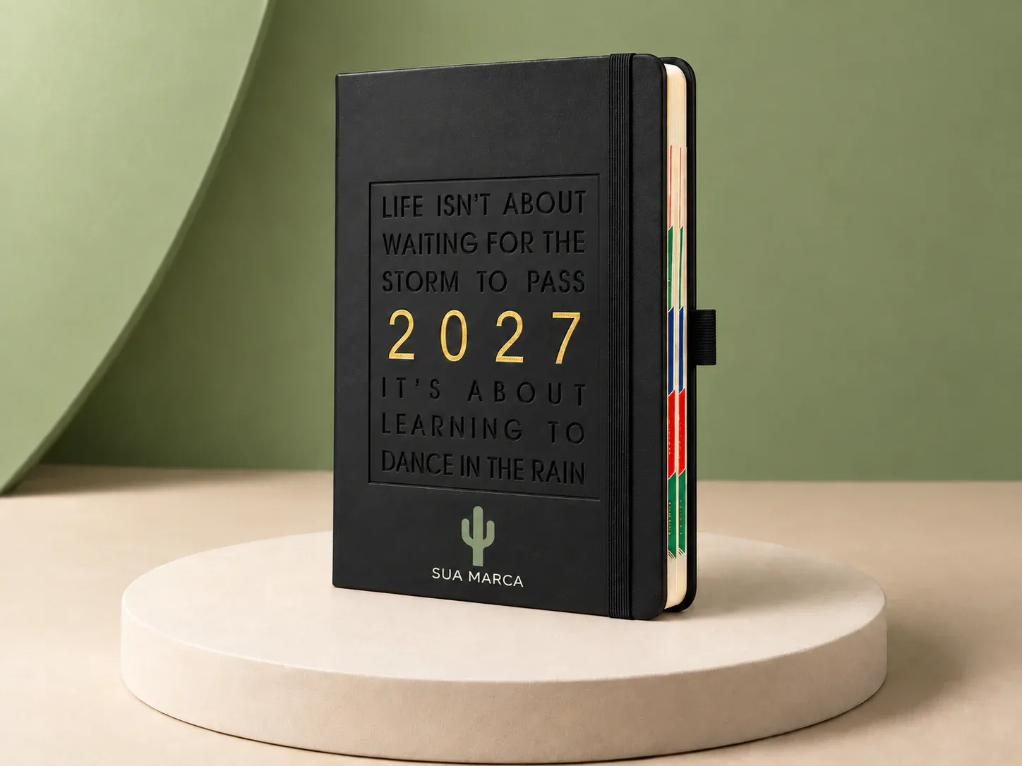 Agenda com elástico e frase na capa, com exemplo de personalização colorida: um cacto e o texto “SUA MARCA” impressos em cor